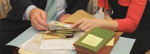 Two people reviewing vintage photos and documents on a table with a green notebook.